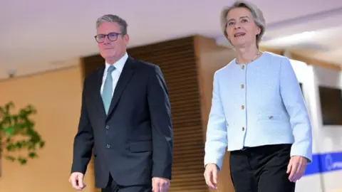 NICOLAS TUCAT/AFP A man in a suit and blue tie strides forward beside a woman in dark trousers and a light blue jacket