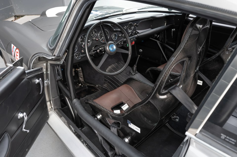 Interior view of an Aston Martin DB4 GT Continuation, showing the dashboard, carbon fiber seats, and steering wheel.