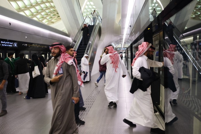 Passengers, including men in traditional Saudi attire, board a train at the King Abdullah Financial District metro station in Riyadh.