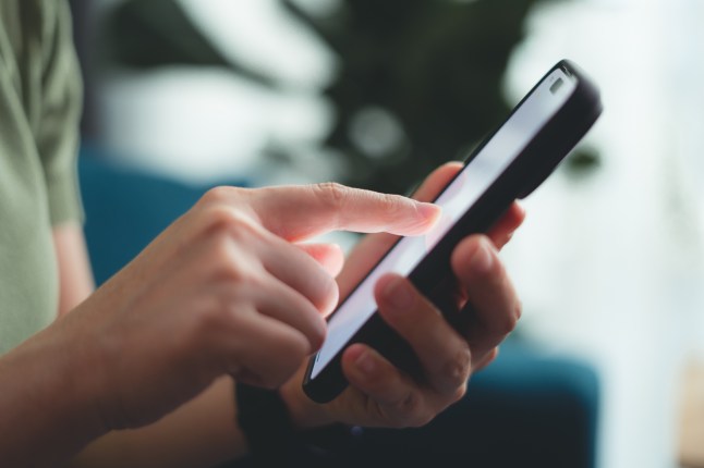 Close-up shot of female hands using smart phone sitting on sofa in living room at home.