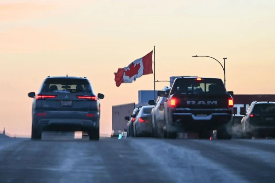 Vehicles stopped at a border crossing with a Canadian flag waving.