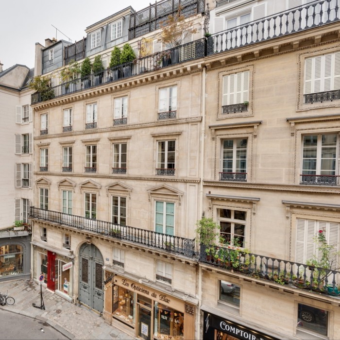 A building with cream-colored stone, wrought-iron balconies adorned with plants, rooftop terraces, and boutique shops at street level