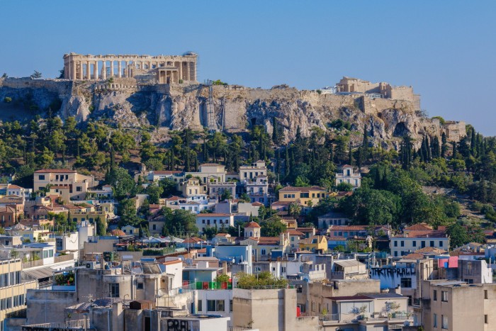 A view of the Acropolis in Athens, Greece, perched on a rocky hill, overlooking a mix of historic and modern buildings