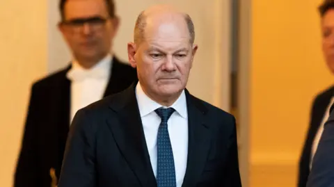 Getty Images German Chancellor Olaf Scholz walks out of the Elysee Palace wearing a dark suit, white shirt and blue tie.