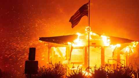 A US flag flies in front of a burning structure in Los Angeles