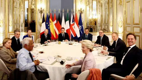 Downing Street European leaders sit around a table in the Elysee Palace with flags in a line behind them. In the middle sits European Council President Antonio Costa and European Commission President Ursula von der Leyen, and from left to right: Italian PM Giorgia Meloni, Dutch PM Dick Schoof, Danish PM Mette Frederiksen, German Chancellor Olaf Scholz, French President Emmanuel Macron, Spanish PM Pedro Sanchez, UK PM Keir Starmer, Polish PM Donald Tusk, and Nato secretary general Mark Rutte.