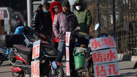 Chinese migrant workers stand near signs advertising their skills as they wait by a street to be hired in Shenyang, in northeastern Liaoning province