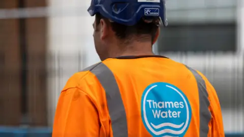 Getty Images The back of a Thames Water worker who is wearing an orange hi-vis top with a blue construction hard hat