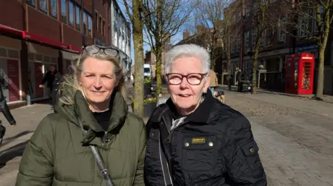 Nicola Tomlinson and Linda Willdig, two retired women in warm coats on Macclesfield market square