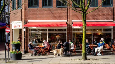 Katerina Antos-Lewis People sitting at a table outside Gail's cafe, one with a golden retriever and a buggy