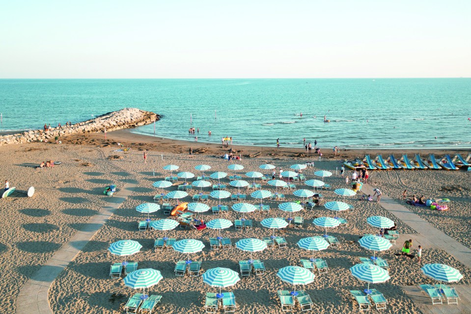 Aerial view of Union Lido beach in Italy with many striped umbrellas and beach chairs.