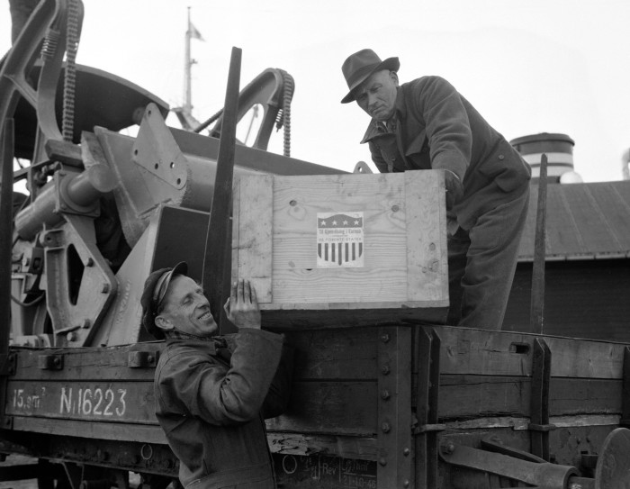 A black-and-white photograph of two men unloading a crate from a wagon