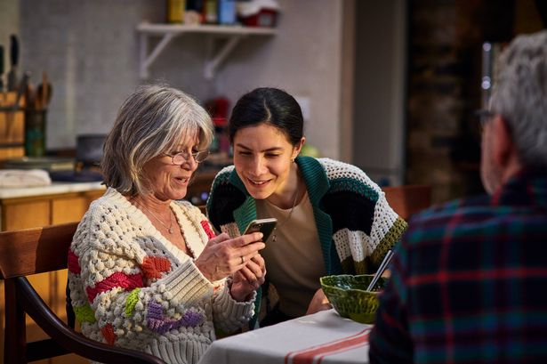 Adopted daughter in her 30's on home visit looking at photos on mother's smart phone and enjoying meal together in kitchen, memories, sharing, wireless technology