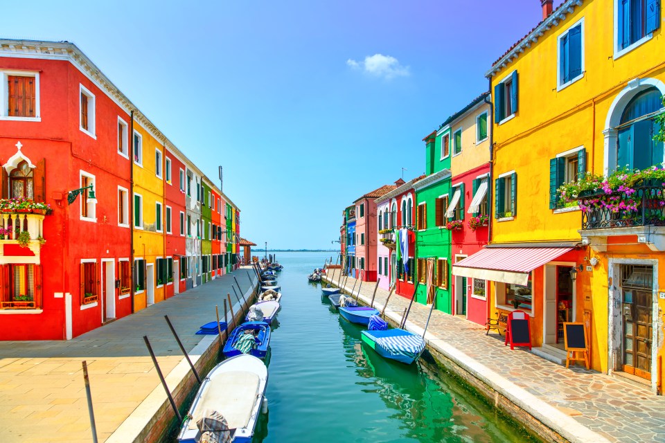 Colorful houses and boats lining a canal in Burano, Italy.