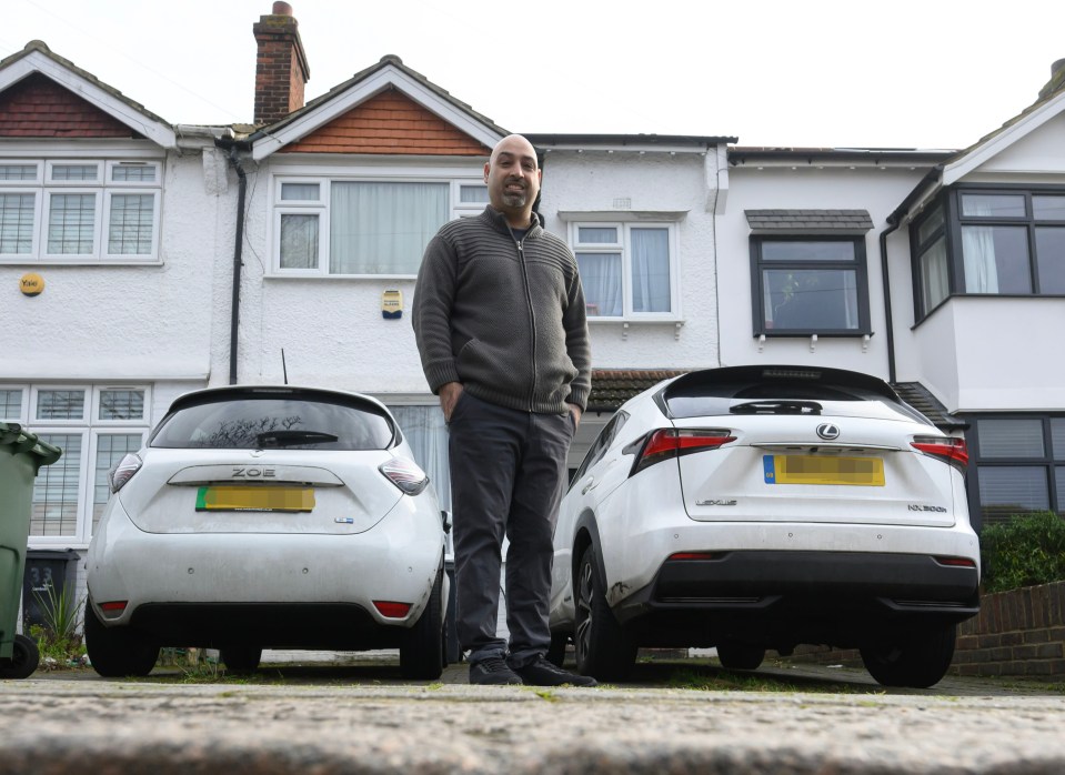 Man standing between two cars parked on his driveway in front of his house.