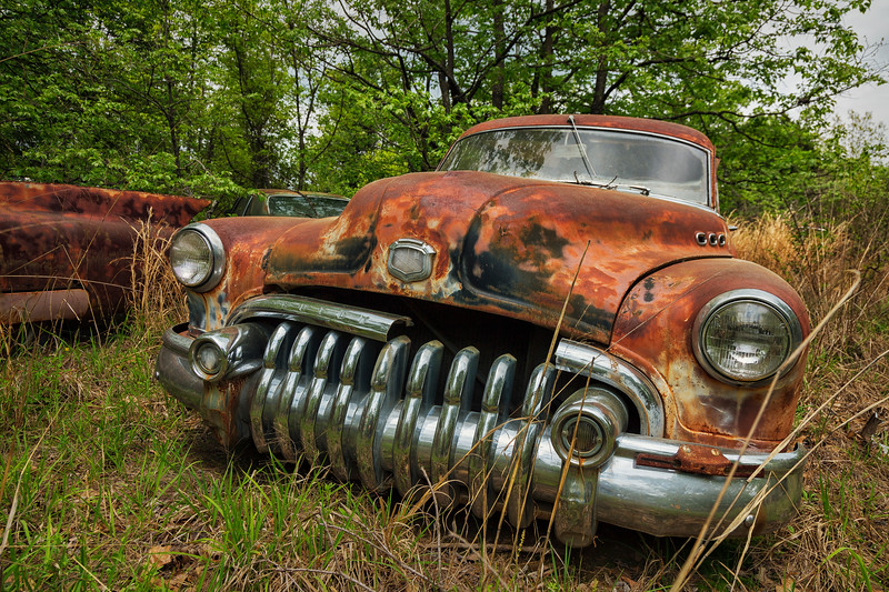 Rusty vintage car in an overgrown field.