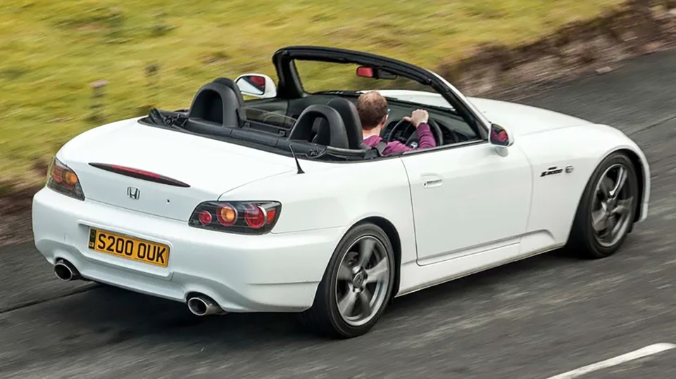 White Honda S2000 convertible driving on a road.