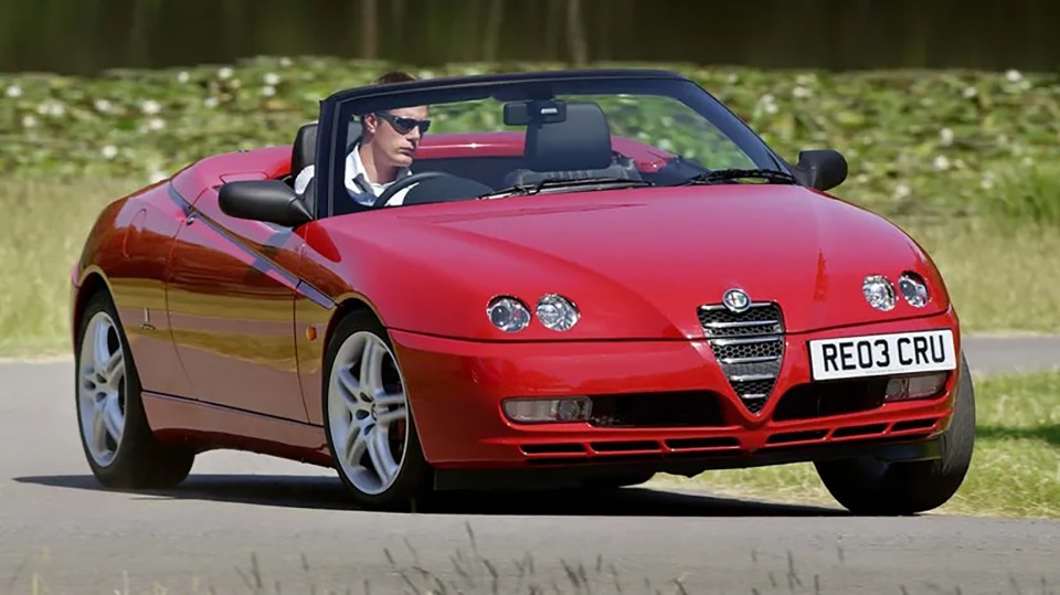 Red Alfa Romeo Spider convertible driving on a road.