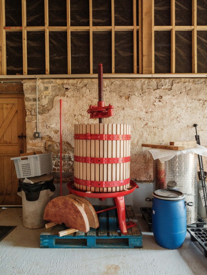 Traditional red and wood wine press on a blue pallet in a rustic room with stone walls and assorted barrels