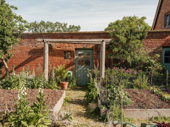 Sunny kitchen garden with raised beds, a green door set in a red brick wall, and flowering plants throughout