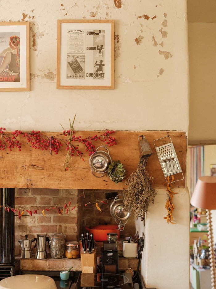 Rustic kitchen with dried herbs, vintage graters, and red berries hanging above a brick and wood stove area