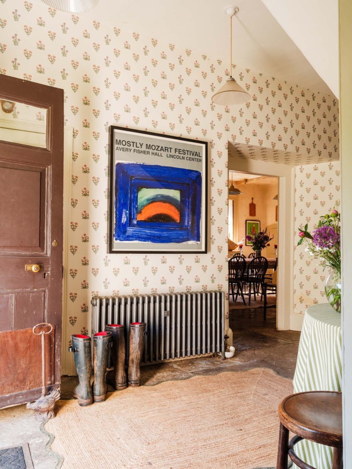 Boot-lined hallway with floral wallpaper, abstract art, and a view into a dining room with wooden chairs