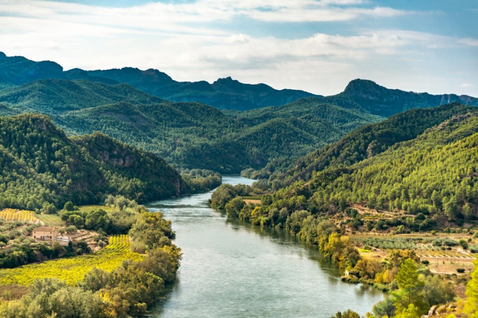 Miravet, Spain - October 10th, 2020: The Ebro River, valley, mountains and forests, against a sunny blue sky with clouds.