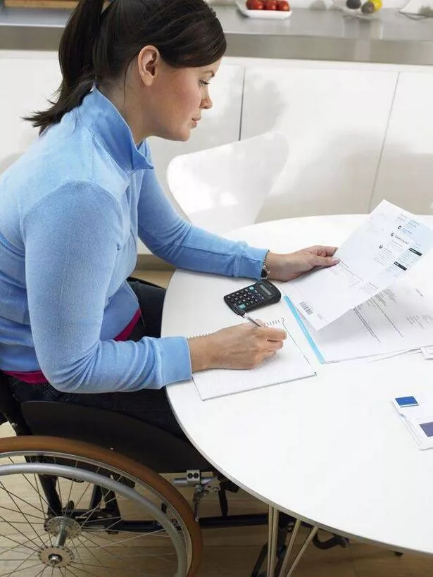 Woman in wheelchair working on accounts at kitchen table, side view