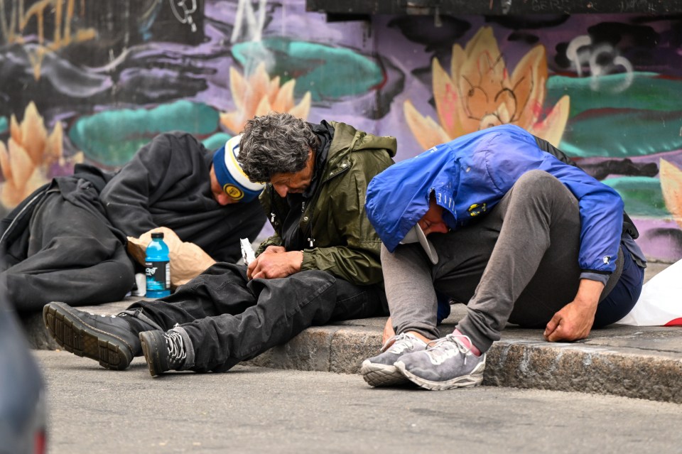 Three homeless people sitting on a city sidewalk.