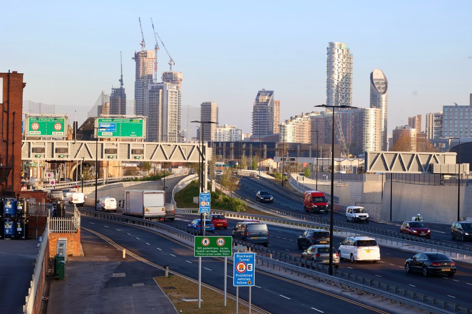 Traffic on a highway near the Blackwall and Silvertown tunnels in London, with a city skyline in the background.